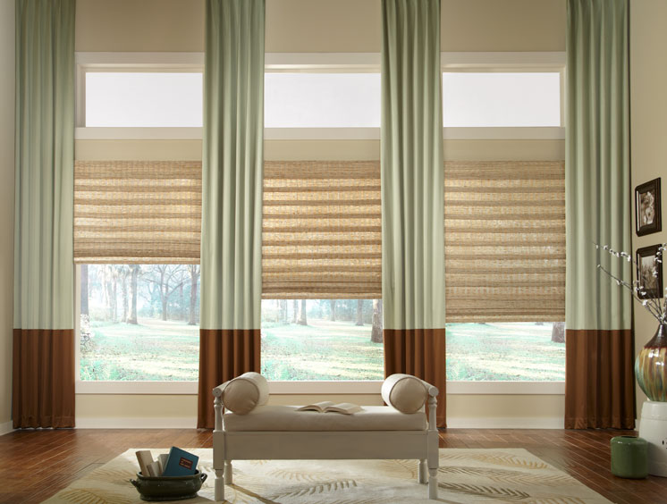 Manh Truc® Woven Wood Shades & Interior Masterpieces® Draperies Light Brown Manh Truc® Woven Wood Shades with light green and dark brown Interior Masterpieces® Draperies haning between them in a room with a beige bench