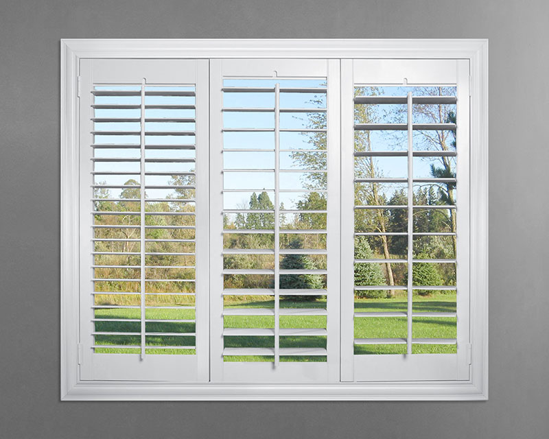Parke® Shutters in 2.5", 3.5" & 4.5" louvers white Parke® Shutters in 2.5", 3.5" & 4.5" louvers in a gray wall with a grassy green field and trees behind