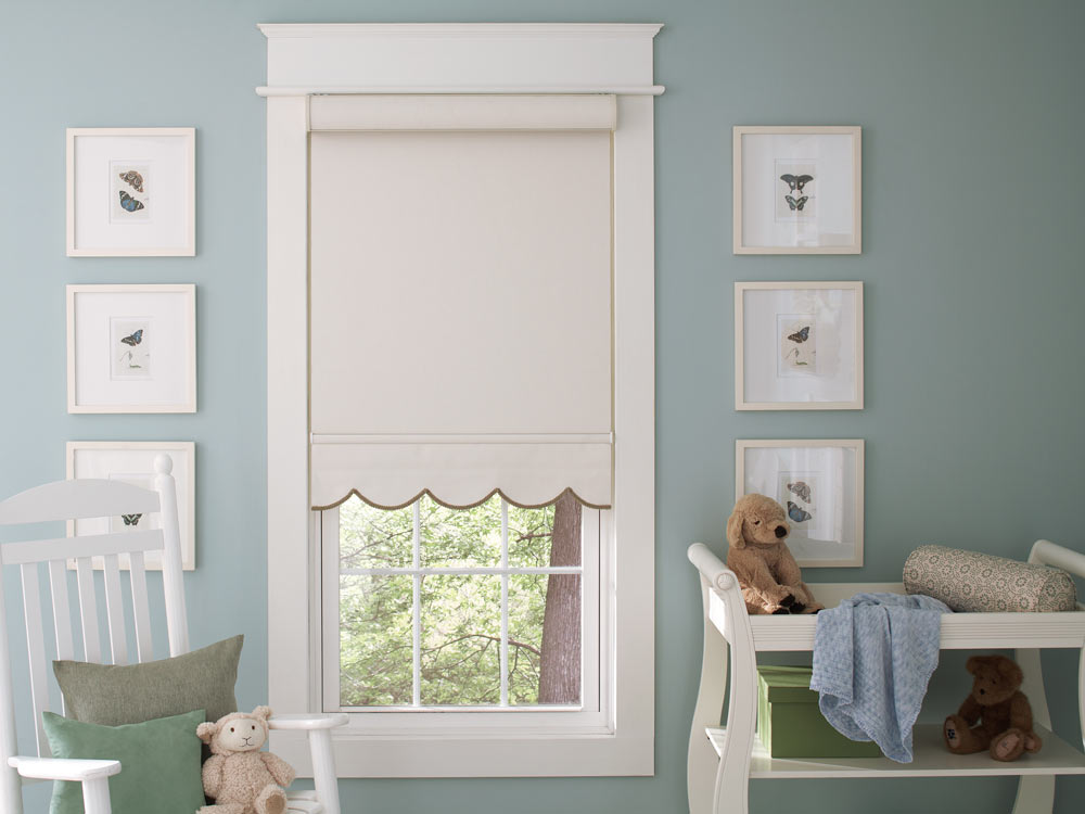 Off white Genesis® Cassette Roller Shade with Scallopped Hem and Brown Embellishment Trim next to a changing station with a couple stuffed animals around