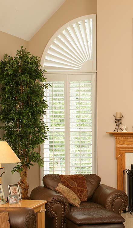 Parke® Shutters with a Quarter Circle Custom Shape off white Parke® Shutters with a Quarter Circle Custom Shape and a tall potted plant in the foreground and a brown chair