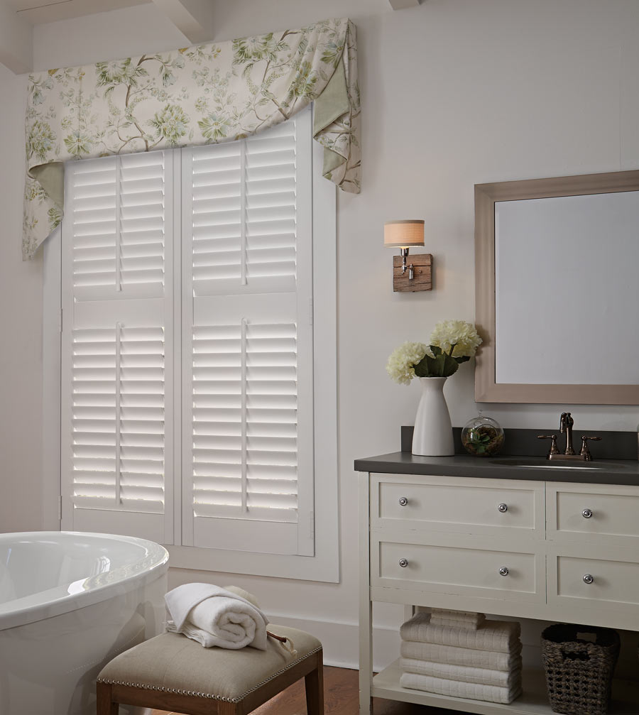 Parke® Shutters & Interior Masterpieces® Fabric Valance white Parke® Shutter with a tan and yellow floral patterened Interior Masterpieces® Fabric Valance in a bathroom with beige walls and a white stand alone tub in the foreground