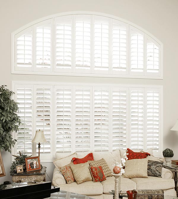 Parke® Shutters & Interior Masterpieces® Custom Pillows Large picture windo with several white Parke® Shutters behind a cream colored couch with tan and red Interior Masterpieces® Custom Pillows